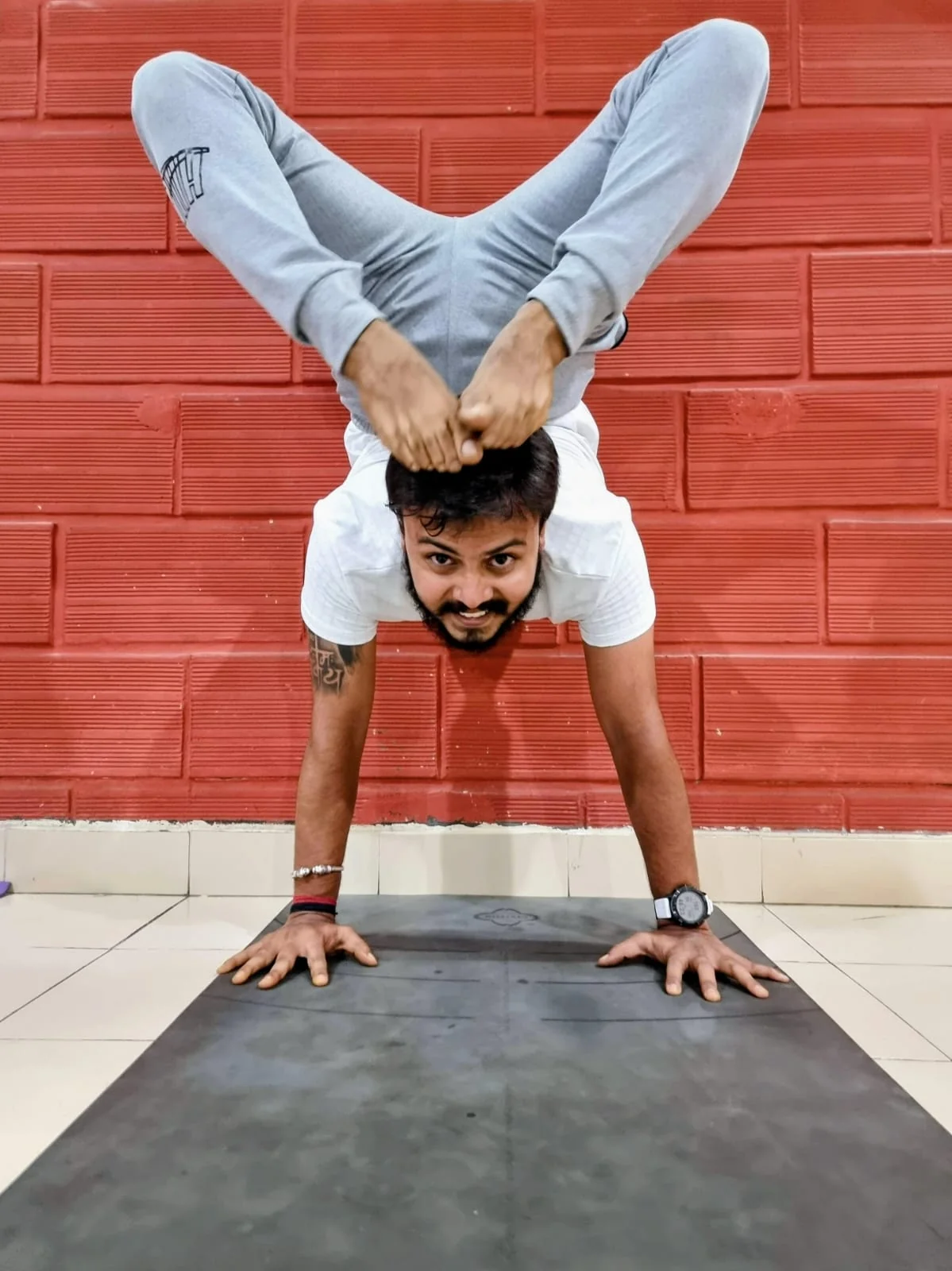 Gandharva holding an advanced arm-balance forward fold against a brick wall